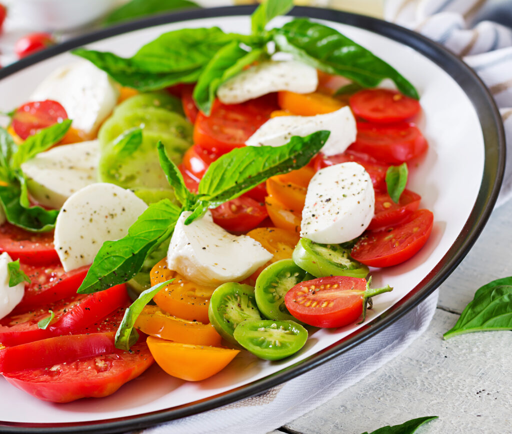 tasty caprese salad with mozzarella cheese and basil leaves 